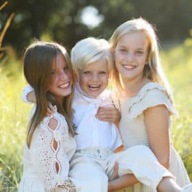 sisters holding younger brother in the air and laughing during family photos in davis california