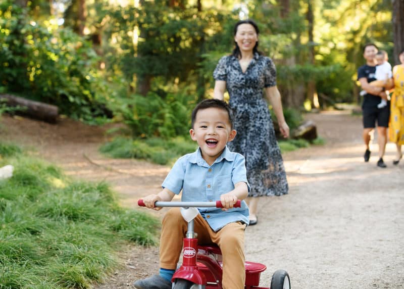 young boy riding a training bike with family following behind and laughing in davis california