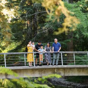 taking family photos on a bridge looking into the water surrounded by trees in davis california