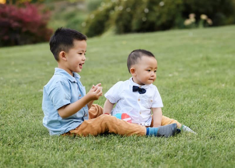 two young brothers sitting on the grass together during family photos in the summer