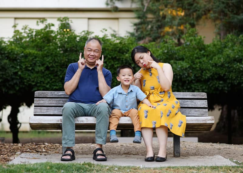 three generations of family sitting on a bench making funny faces during family photos