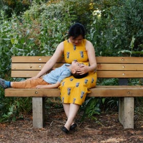 mom sitting on a bench with young son laying in her lap during summer family photos in davis ca