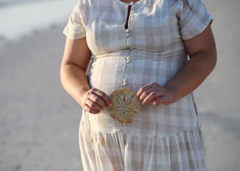 holding a sand dollar next to a woman's pregnant belly during family photos in florida