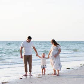 family of three holding hands and walking along the beach in florida during family photos