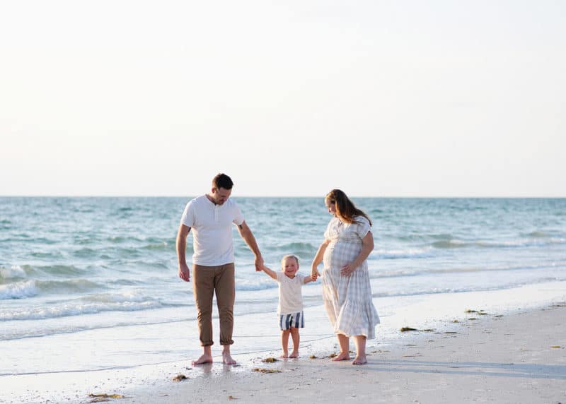 family of three holding hands and walking along the beach in florida during family photos