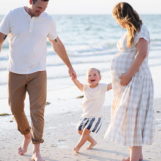 family of three holding hands on the beach and laughing together