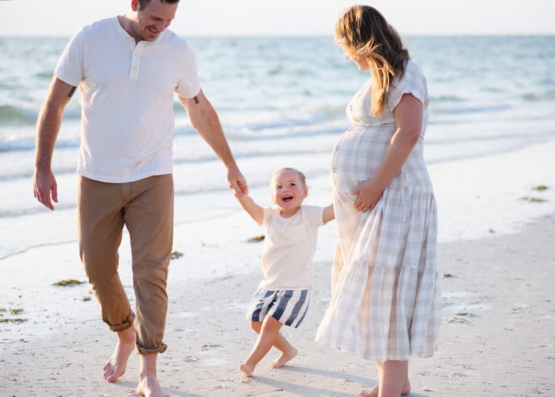 family of three holding hands on the beach and laughing together