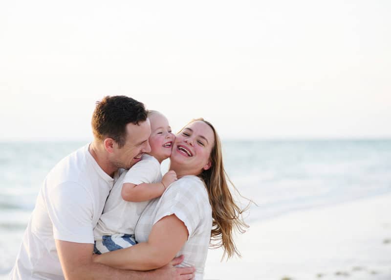 family of three snuggling on the beach on vacation in florida