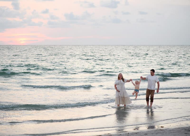 family of three walking in the water on the beach in florida during family maternity photos