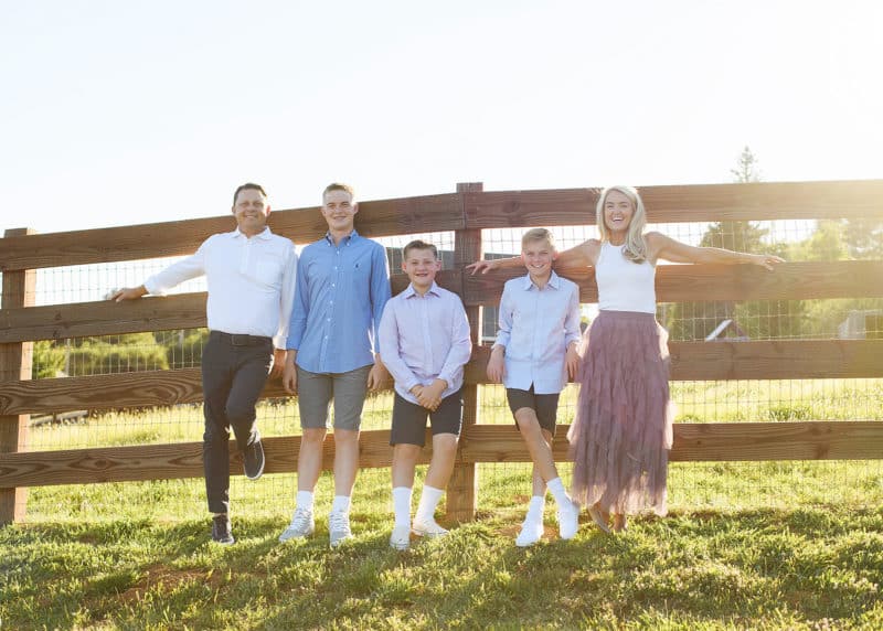 mom and dad with three teenage boys standing in front of a wooden fence during golden hour in newcastle california