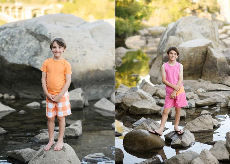 young boys standing on rocks and smiling at the camera in pink and yellow swimsuits during family photo session at folsom lake