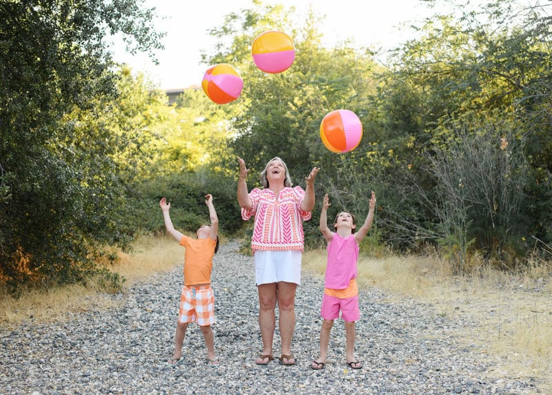 mom with two sons throwing beach balls up in the air during family photo session at folsom lake