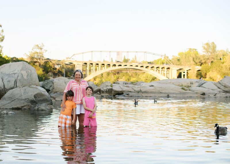 mom with two young boys standing in folsom lake with the bridge behind them during golden hour