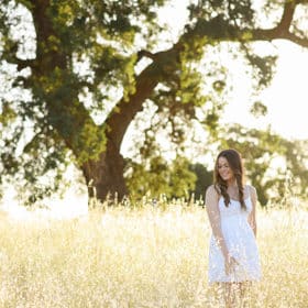 senior in high school wearing a white dress in a field with an oak tree in sacramento california