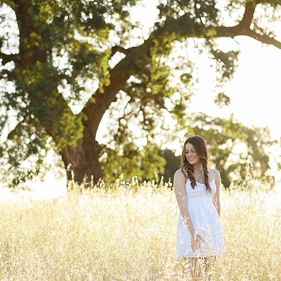 senior in high school wearing a white dress in a field with an oak tree in sacramento california