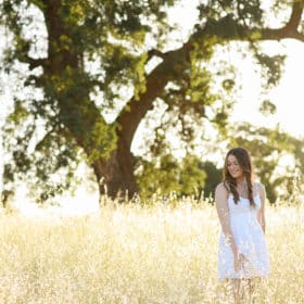 senior in high school wearing a white dress in a field with an oak tree in sacramento california