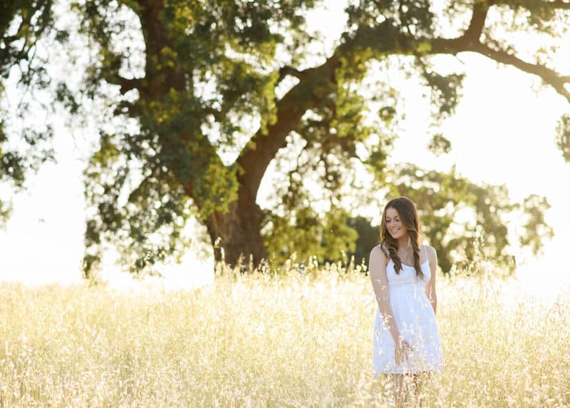 senior in high school wearing a white dress in a field with an oak tree in sacramento california