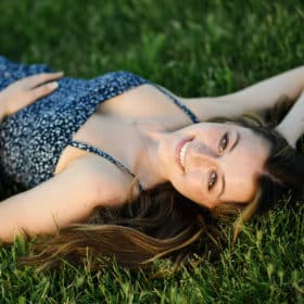 taking senior portraits laying in the grass wearing a blue dress in sacramento california