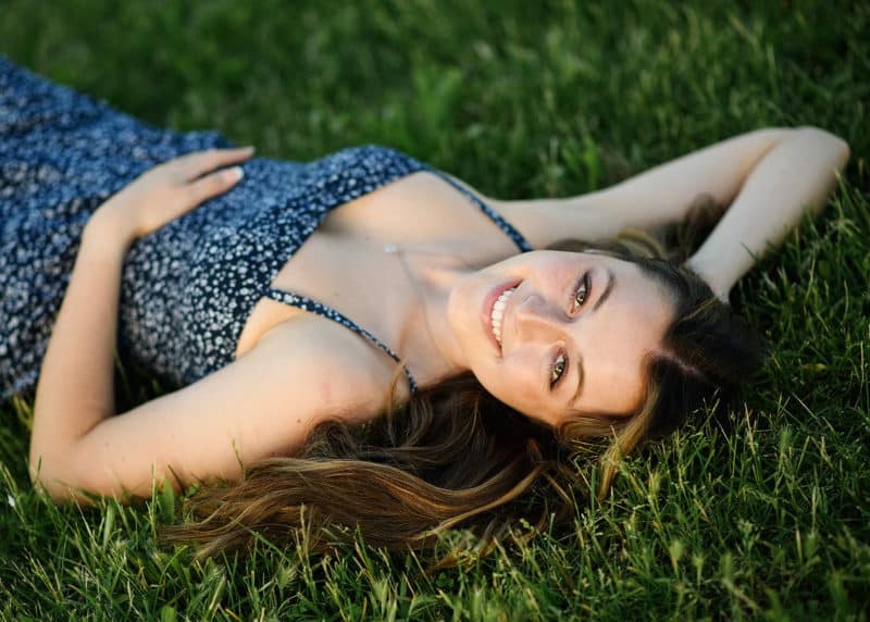 taking senior portraits laying in the grass wearing a blue dress in sacramento california