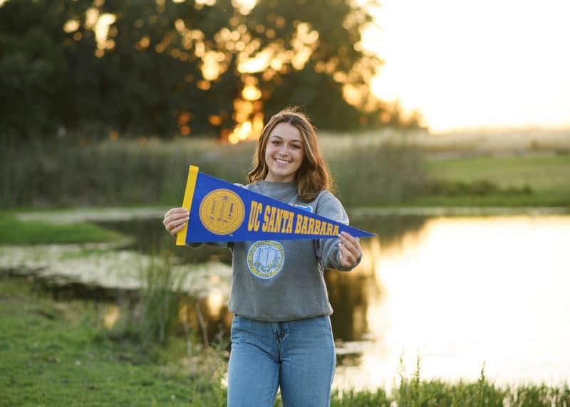 taking senior portraits holding a UC Santa Barbara flag during golden hour in Sacramento CA