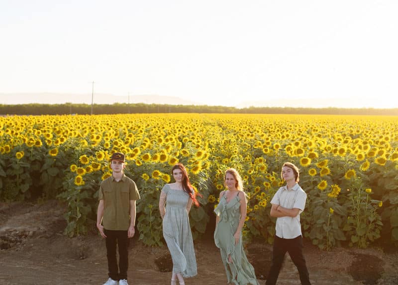 mom with three grown children standing in a golden field of sunflowers in dixon california