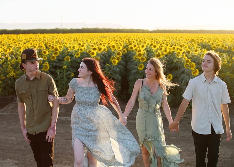 holding hands and walking toward the photographer during family photo session in the sunflower fields of dixon california