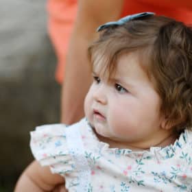 baby girl looking to the side while mom stands her up during family photo session in granite bay california