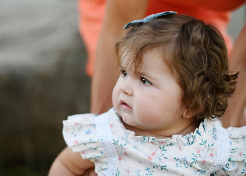 baby girl looking to the side while mom stands her up during family photo session in granite bay california