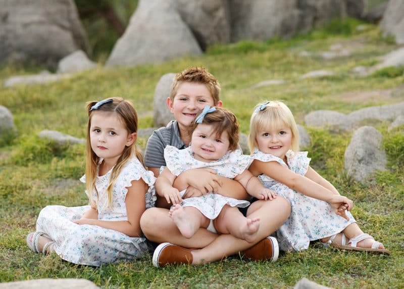 big brother with three younger sisters sitting on the grass taking family photographs in granite bay california