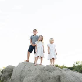 three young kids standing on rocks and smiling during summer photography session in granite bay california