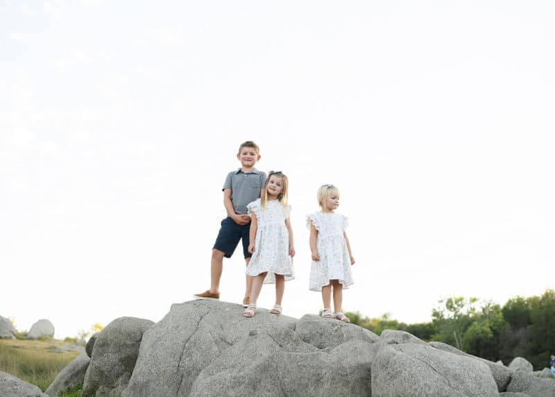 three young kids standing on rocks and smiling during summer photography session in granite bay california