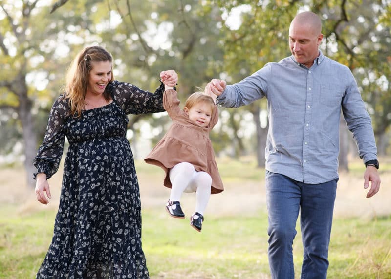 mom and dad swinging young daughter during maternity session with a folsom family photographer