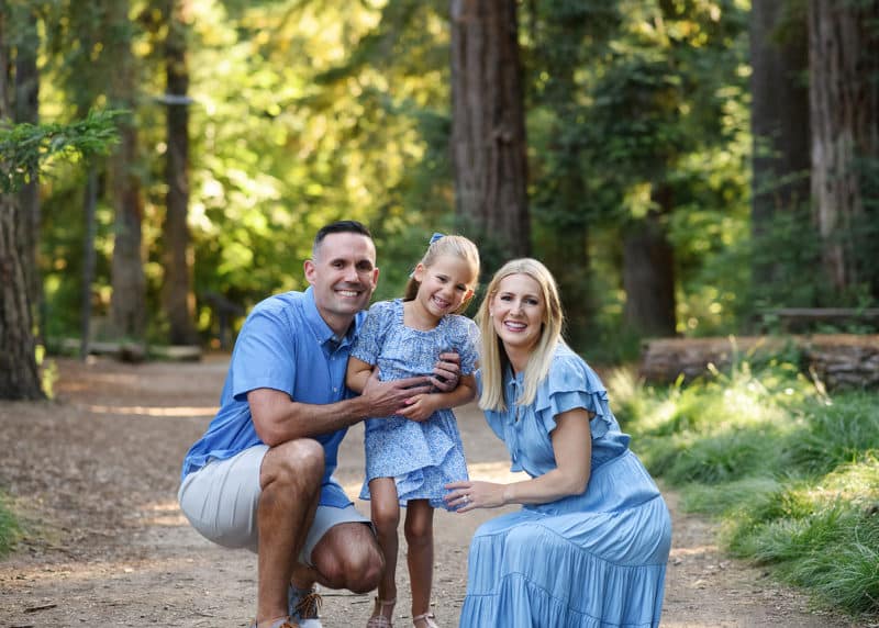 mom and dad with young daughter looking at the photographer and laughing together in davis california