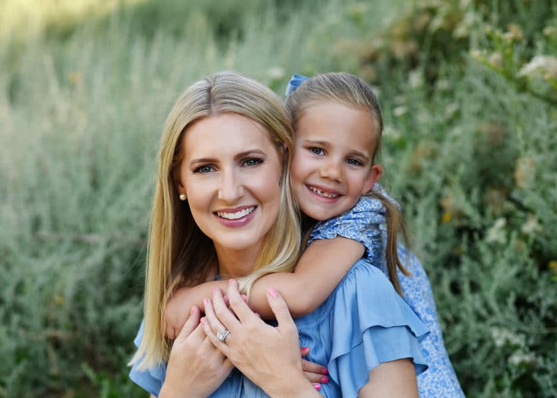 young daughter hugging mom from behind and looking at the photographer during Davis family photo session