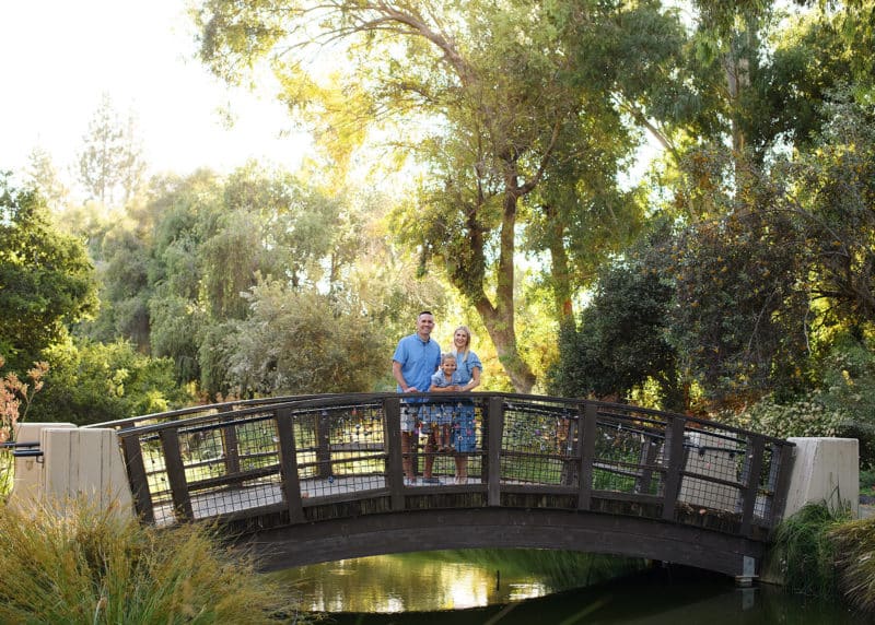 family of three standing on a bridge in a park in davis california surrounded by redwoods