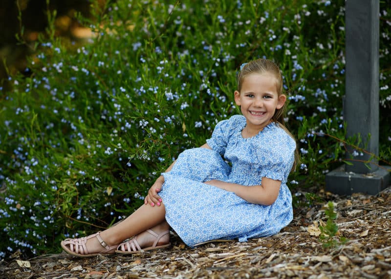 young girl sitting on the ground with wildflowers and looking at the photographer during davis family photo shoot