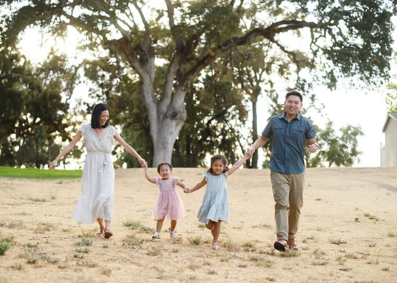 family of four walking hand in hand in front of an oak tree during family photography session in sacramento california