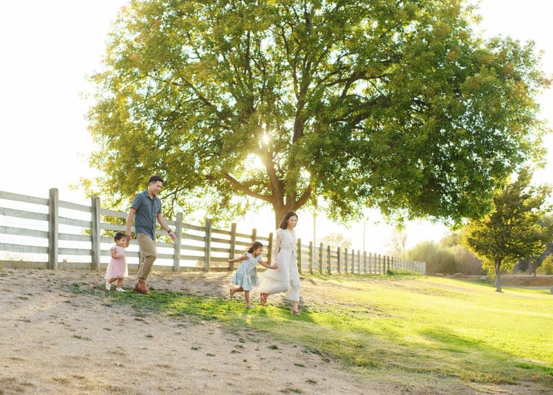 family of four walking in front of a big oak tree during session with photographer in sacramento california