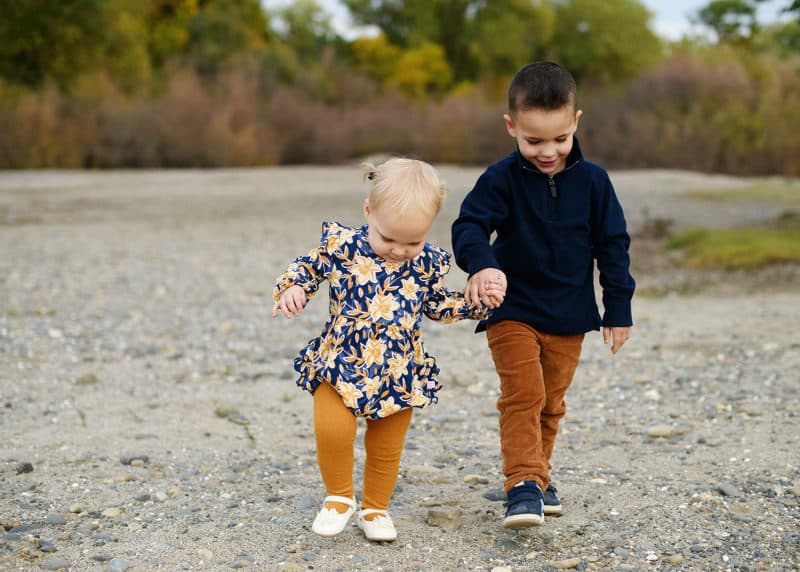 young brother and sister holding hands and walking by the river in sacramento california