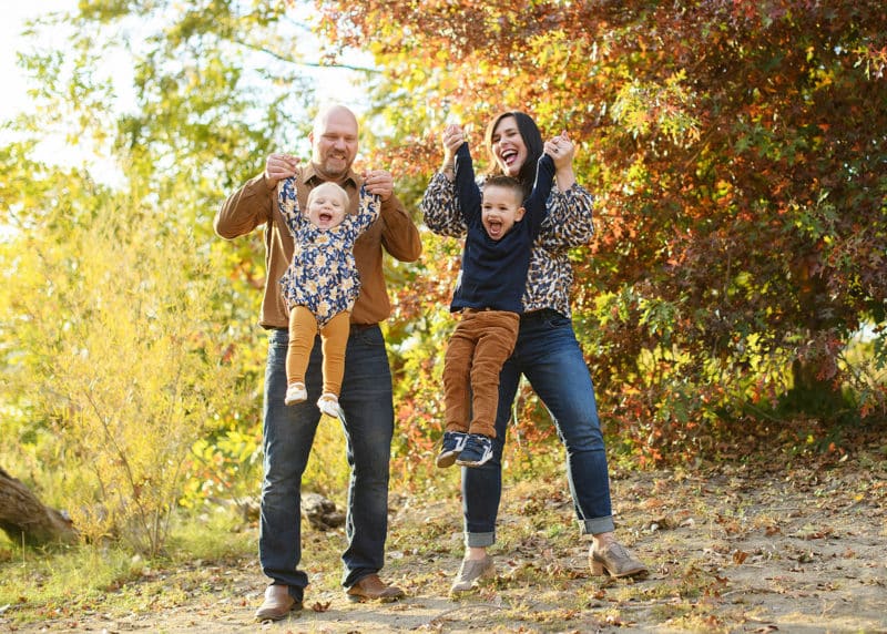 family of four wearing fall clothes and smiling in front of big trees during photos in sacramento california