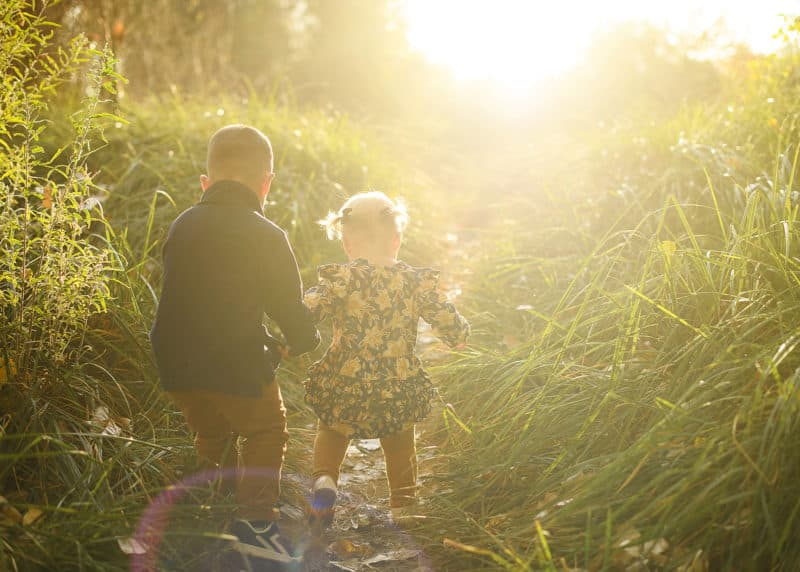 brother and sister holding hands and walking in the long grass during fall photos in sacramento california