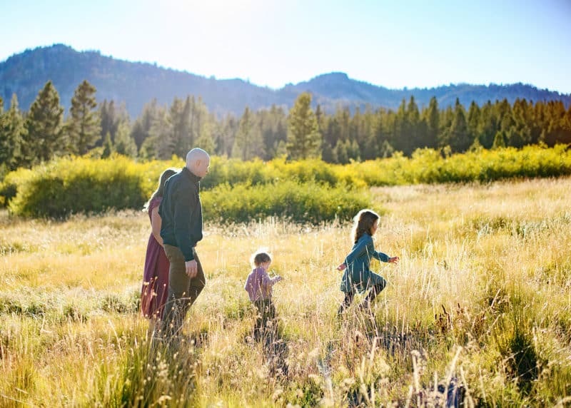 lake tahoe photographer taking photos of a family of four walking in a field with the mountains in the distance