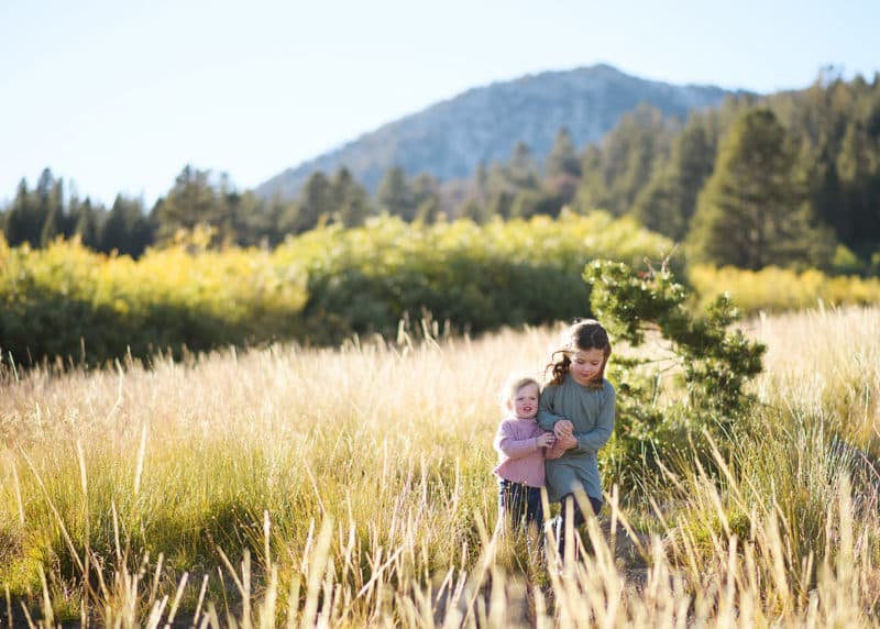 two young sisters holding hands walking through a field by the mountains of lake tahoe california