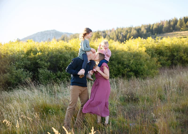 mom and dad kissing with young daughters on their shoulders, lake tahoe photographer, jill carmel photography