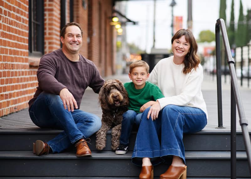 family of three sitting on steps in front of a brick building with the family dog in downtown sacramento california 