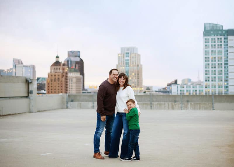 family of three standing on a rooftop in downtown sacramento california with photographer taking family pictures