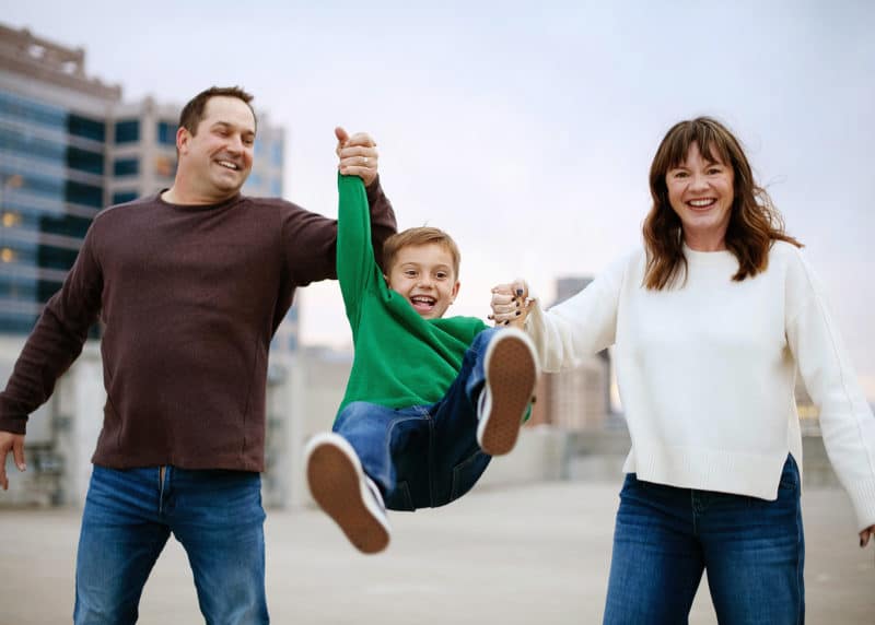 mom and dad swinging young son by the arms while photographer takes pictures in downtown sacramento california