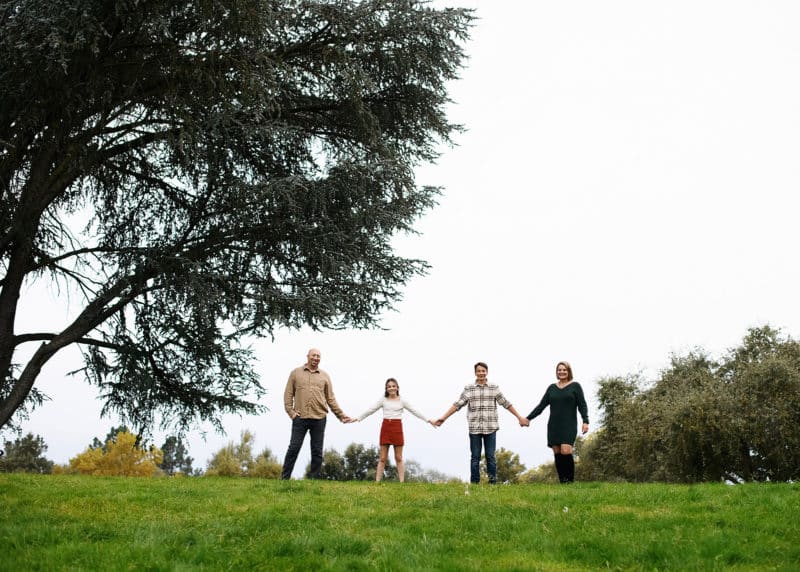 family of four holding hands on a hill during fall photo session with jill carmel photography in sacramento california