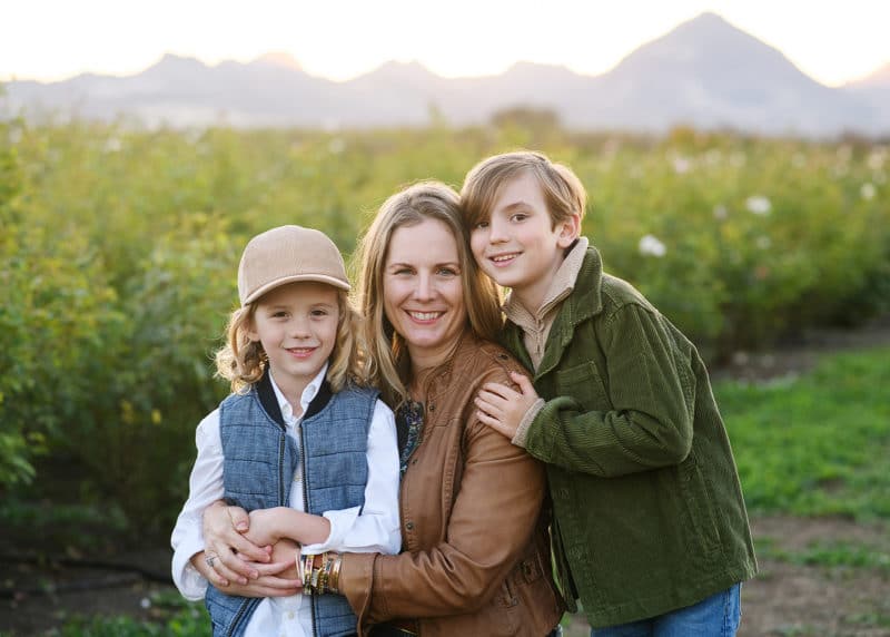 mom with two young sons taking pictures in front of rose bushes with mountains in the background