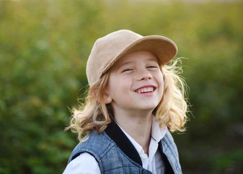 young boy wearing a hat and laughing at the photographer during family photos in yuba city california